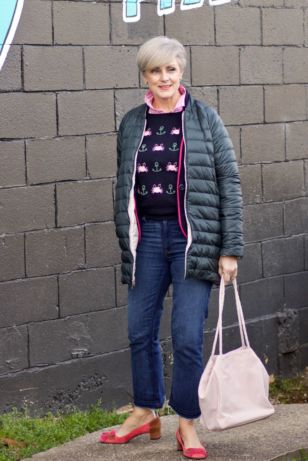 beth from Style at a Certain Age wears a puffer jacket, navy blue knit blazer, novelty sweater, pink gingham check shirt and blue jeans