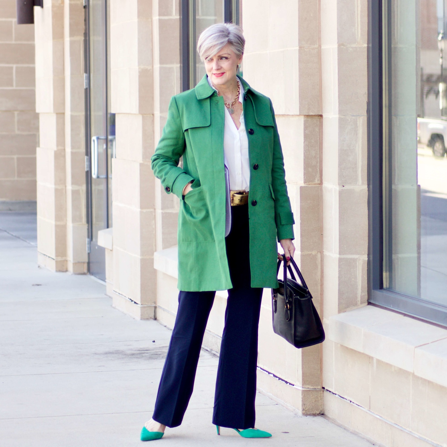 beth from Style at a Certain Age wears a Ann Taylor green trench coat, navy trousers, white essential shirt, knit striped blazer, and green suede pumps.