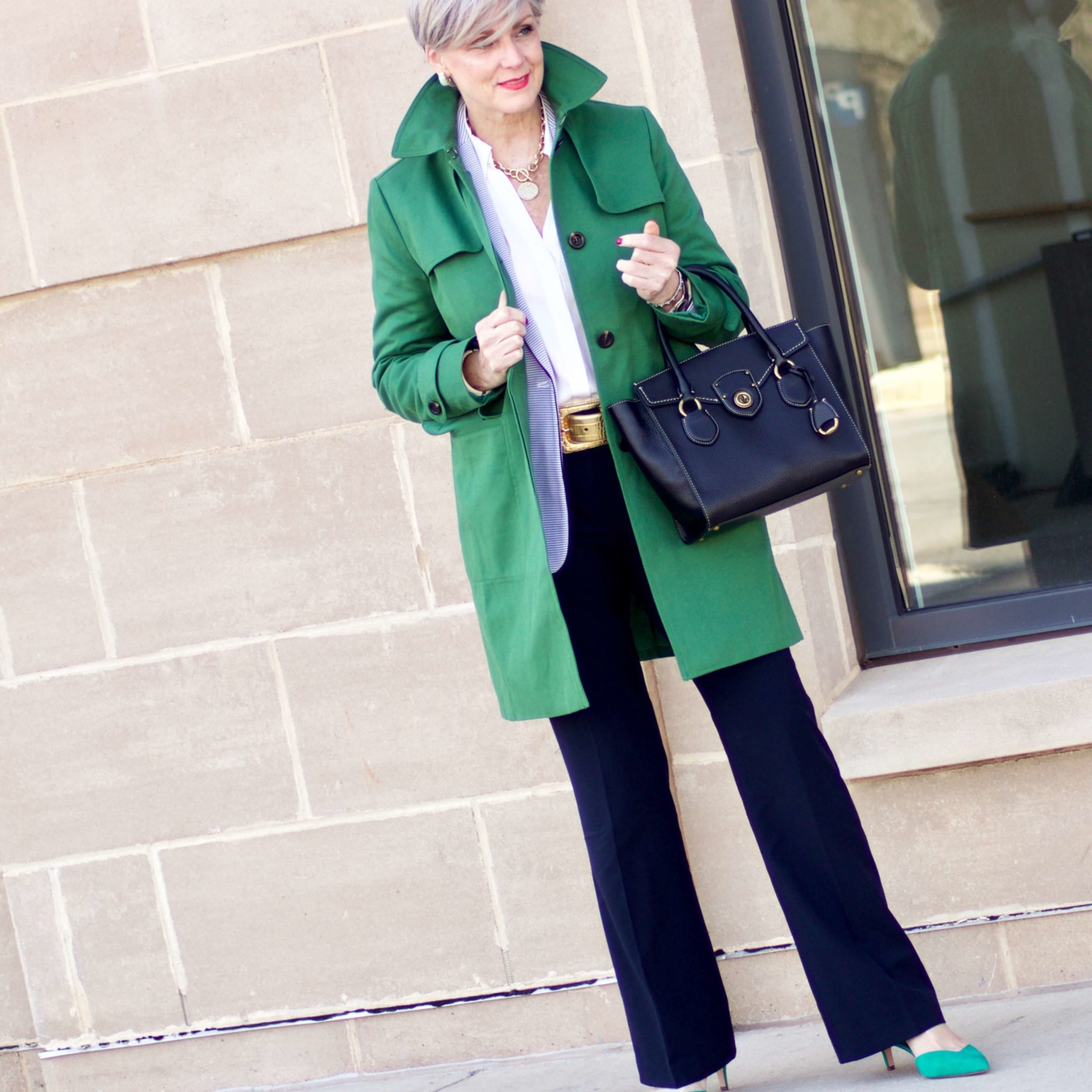 beth from Style at a Certain Age wears a Ann Taylor green trench coat, navy trousers, white essential shirt, knit striped blazer, and green suede pumps.