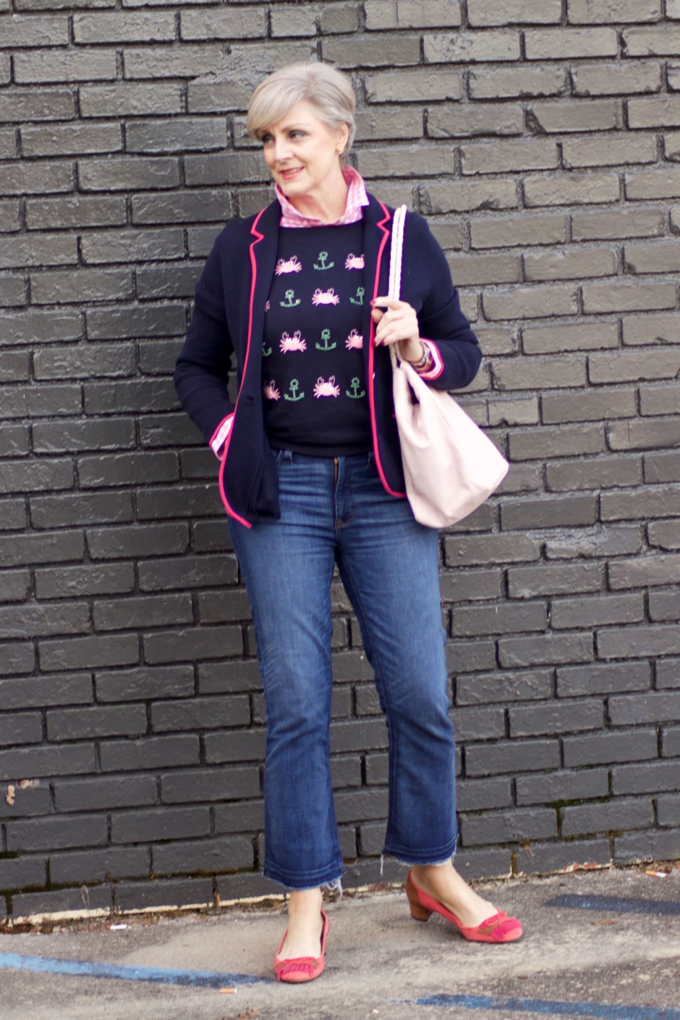 beth from Style at a Certain Age wears a puffer jacket, navy blue knit blazer, novelty sweater, pink gingham check shirt and blue jeans