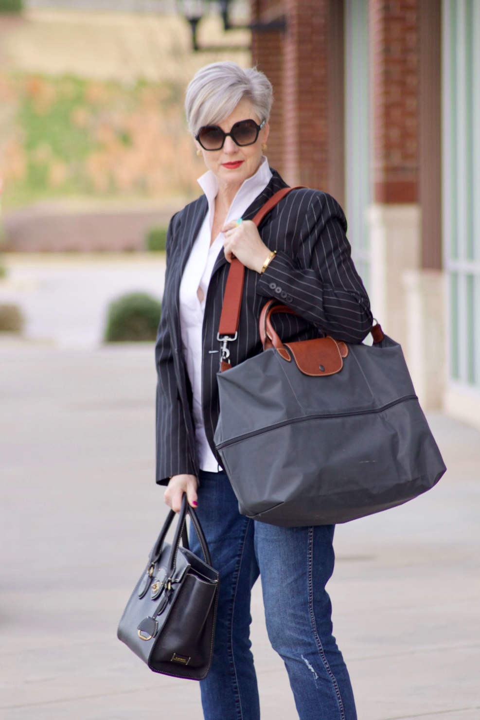 beth from Style at a Certain Age travels in style in a pinstripe blazer, white button down, blue jeans, and black slides