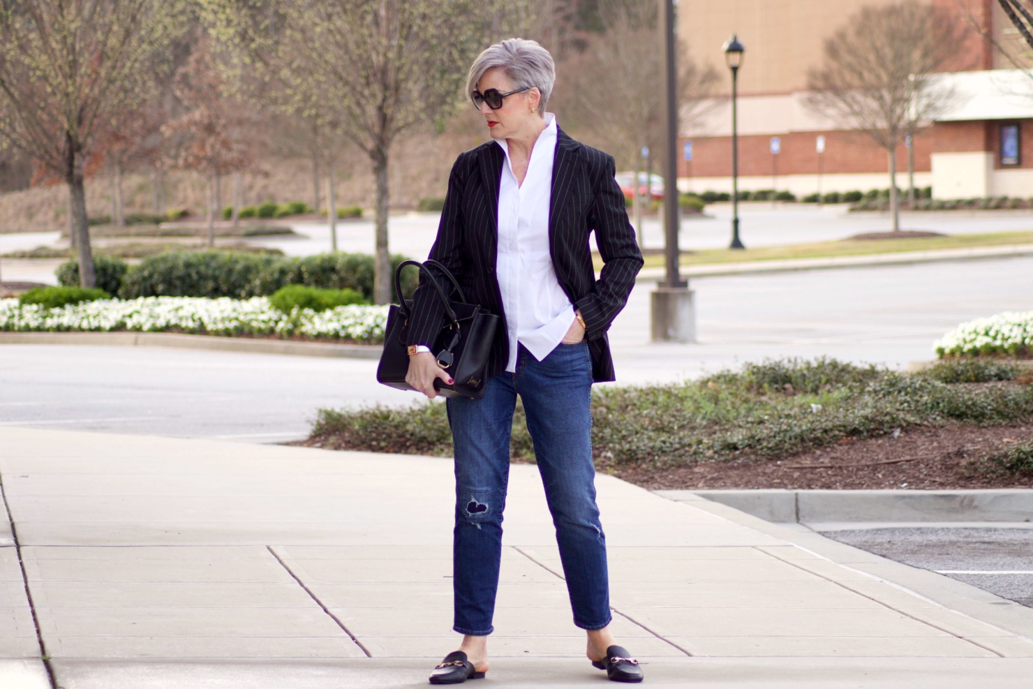 beth from Style at a Certain Age travels in style in a pinstripe blazer, white button down, blue jeans, and black slides