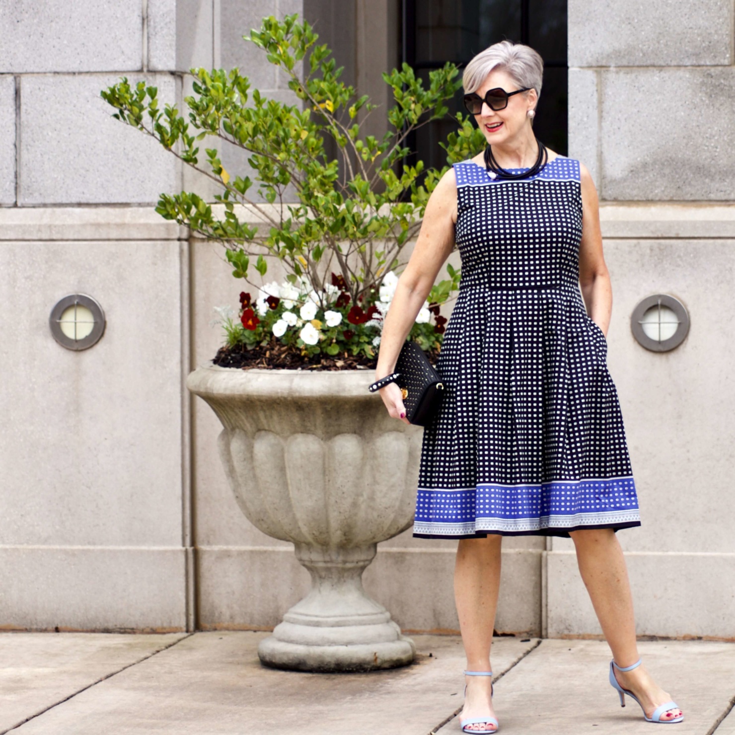 beth from Style at a Certain Age wears a fit and flare dress, kitten heel sandals, and a black clutch handbag