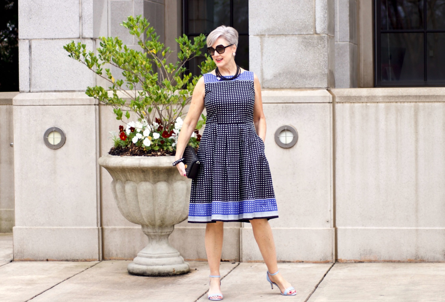 beth from Style at a Certain Age wears a fit and flare dress, kitten heel sandals, and a black clutch handbag