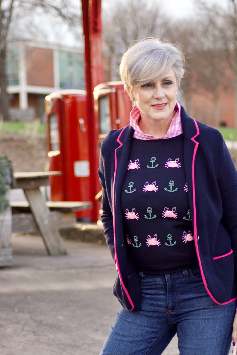 beth from Style at a Certain Age wears a puffer jacket, navy blue knit blazer, novelty sweater, pink gingham check shirt and blue jeans