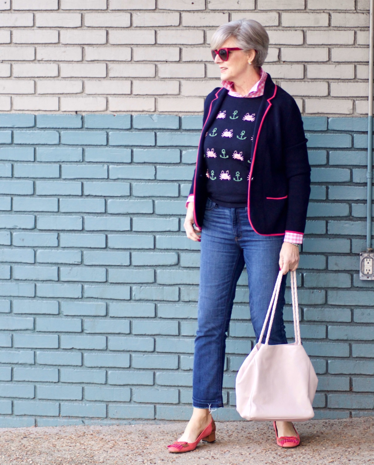 beth from Style at a Certain Age wears a puffer jacket, navy blue knit blazer, novelty sweater, pink gingham check shirt and blue jeans