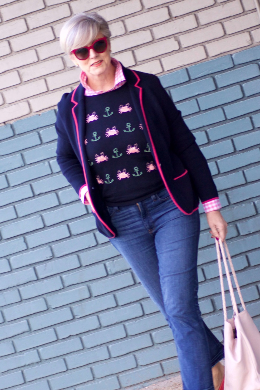 beth from Style at a Certain Age wears a puffer jacket, navy blue knit blazer, novelty sweater, pink gingham check shirt and blue jeans
