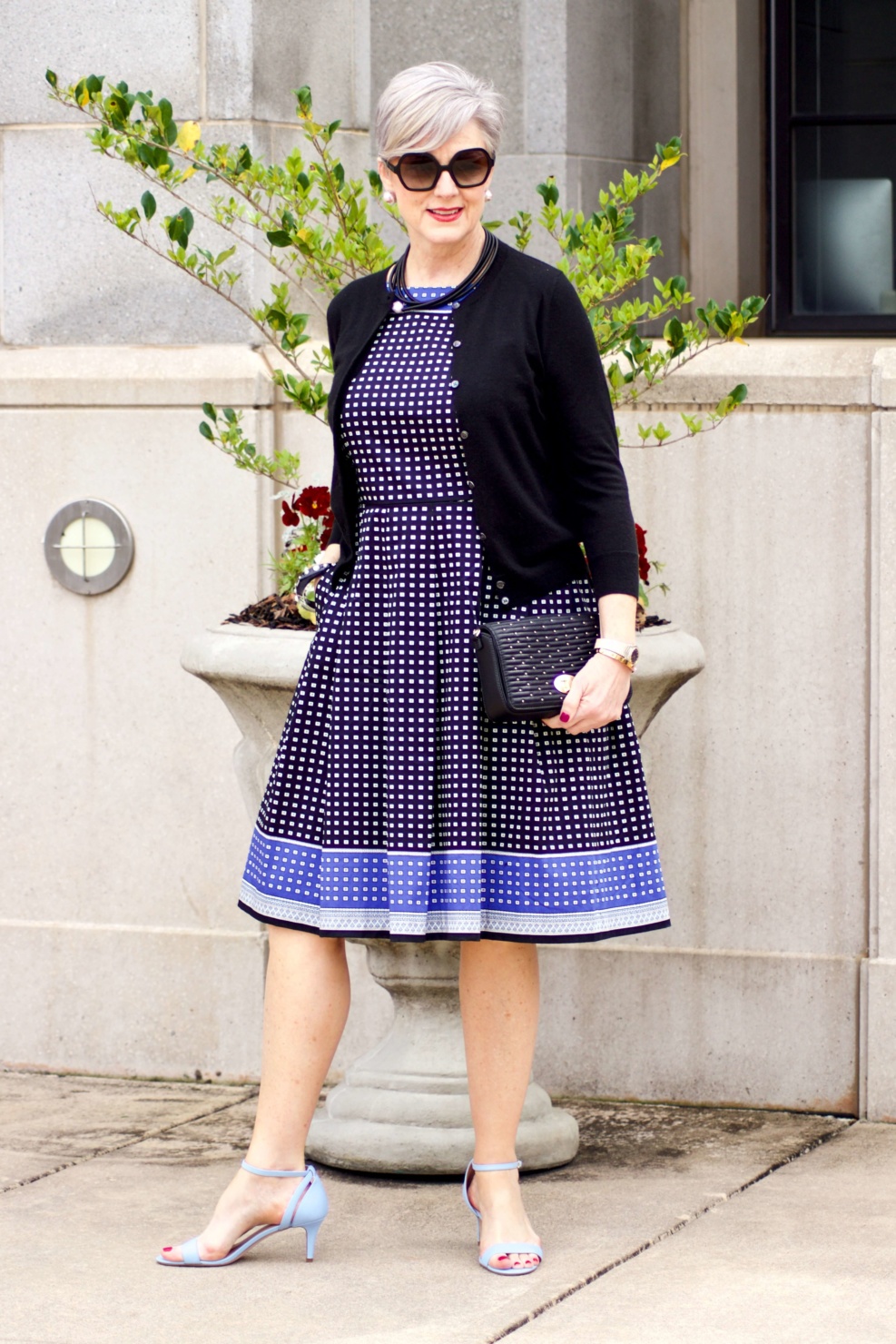 beth from Style at a Certain Age wears a fit and flare dress, kitten heel sandals, and a black clutch handbag