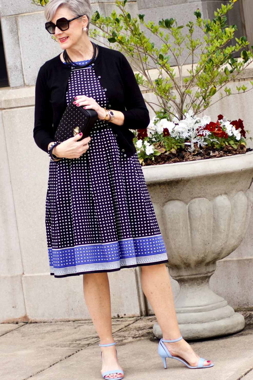 beth from Style at a Certain Age wears a fit and flare dress, kitten heel sandals, and a black clutch handbag