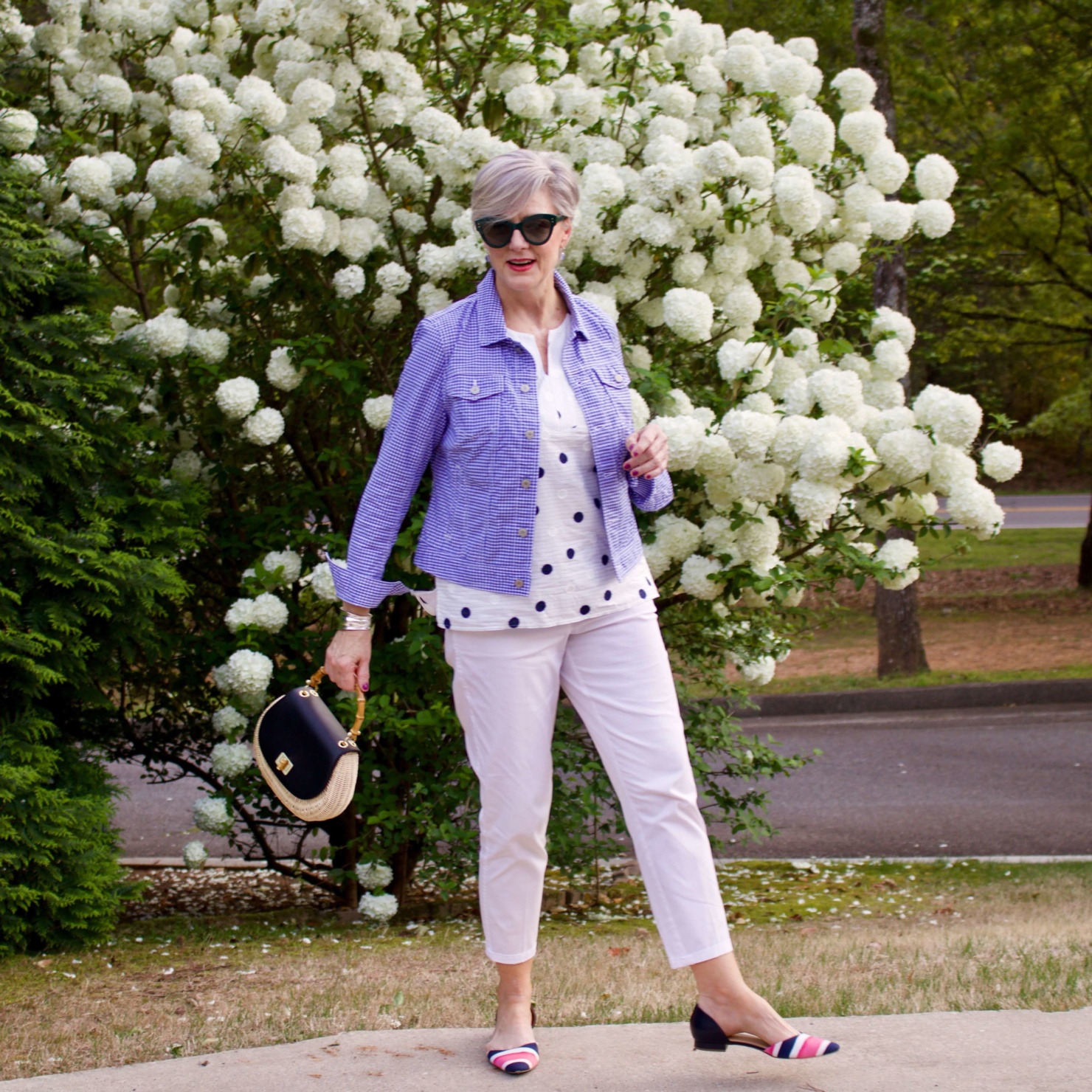 beth from Style at a Certain Age wears a gingham jean jacket, polka dot top, white chinos and wicker handbag