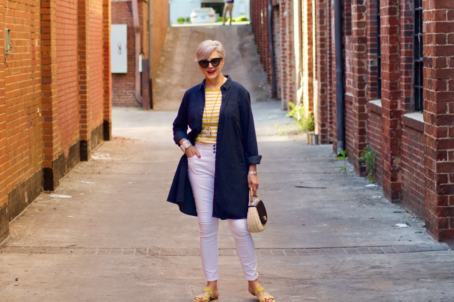 beth from Style at a Certain Age wears a denim duster, striped tee, white denim, suede sandals and wicker handbag