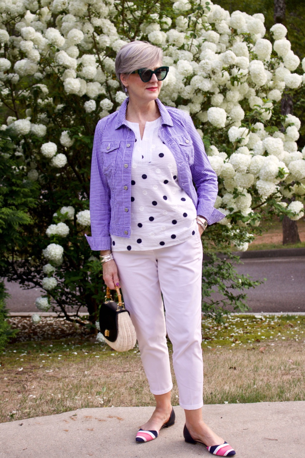 beth from Style at a Certain Age wears a gingham jean jacket, polka dot top, white chinos and wicker handbag