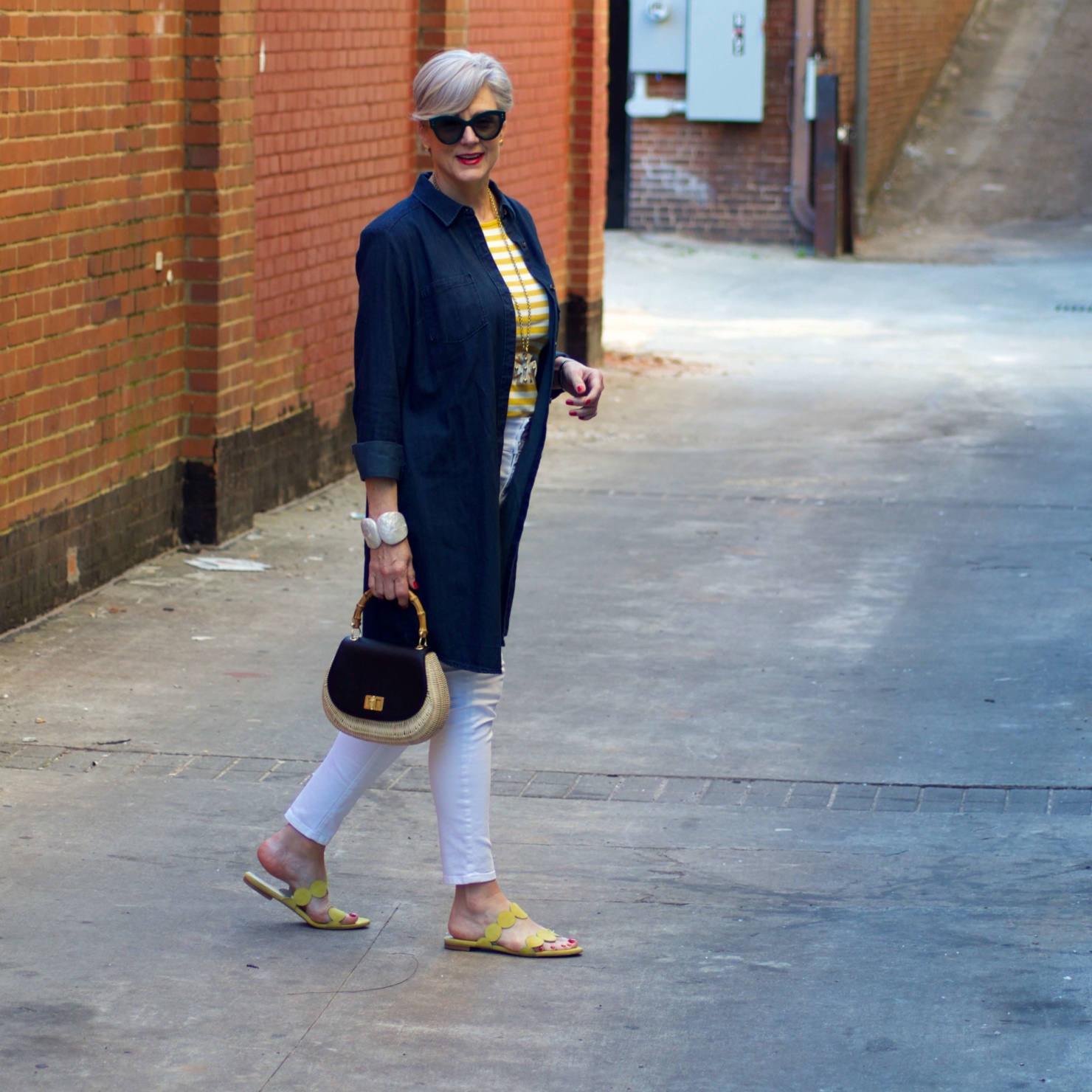 beth from Style at a Certain Age wears a denim duster, striped tee, white denim, suede sandals and wicker handbag