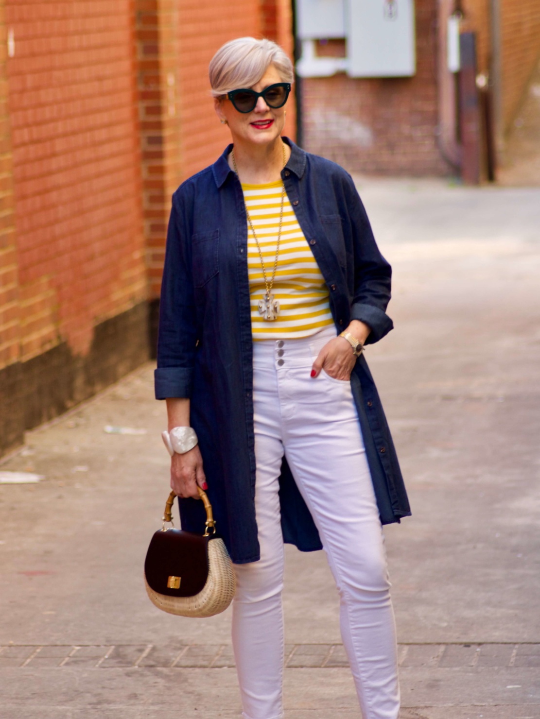 beth from Style at a Certain Age wears a denim duster, striped tee, white denim, suede sandals and wicker handbag