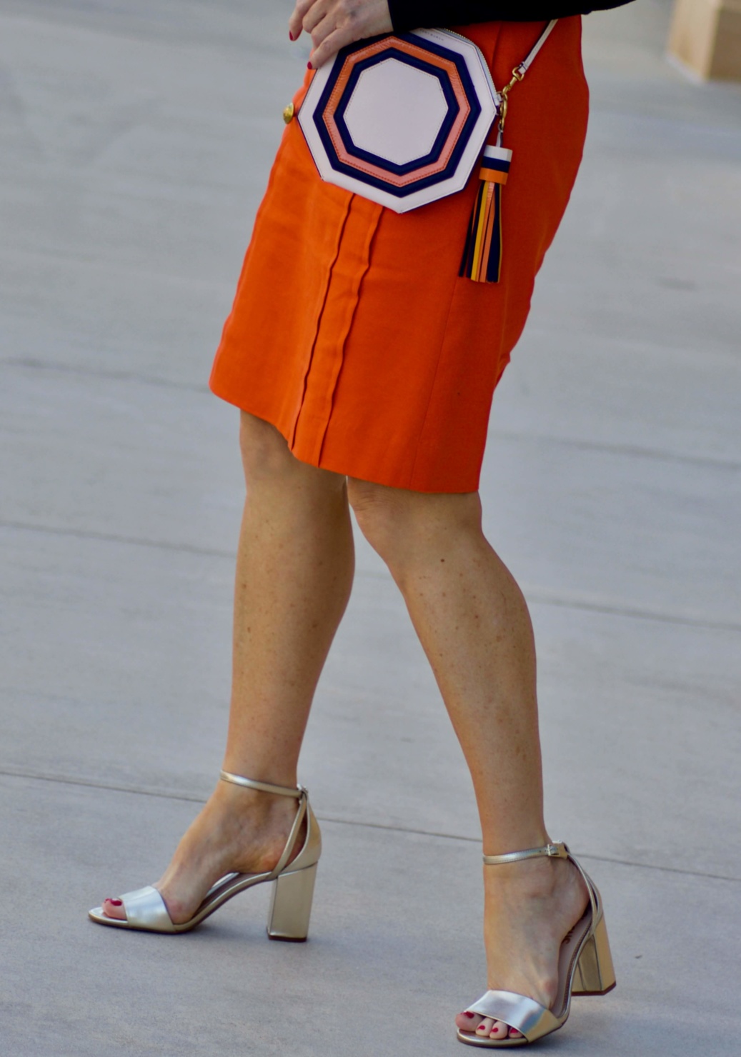 beth from Style at a Certain Age wears a J.Crew orange skirt, blue tee, gold sandals, and Tory Burch mini bag.