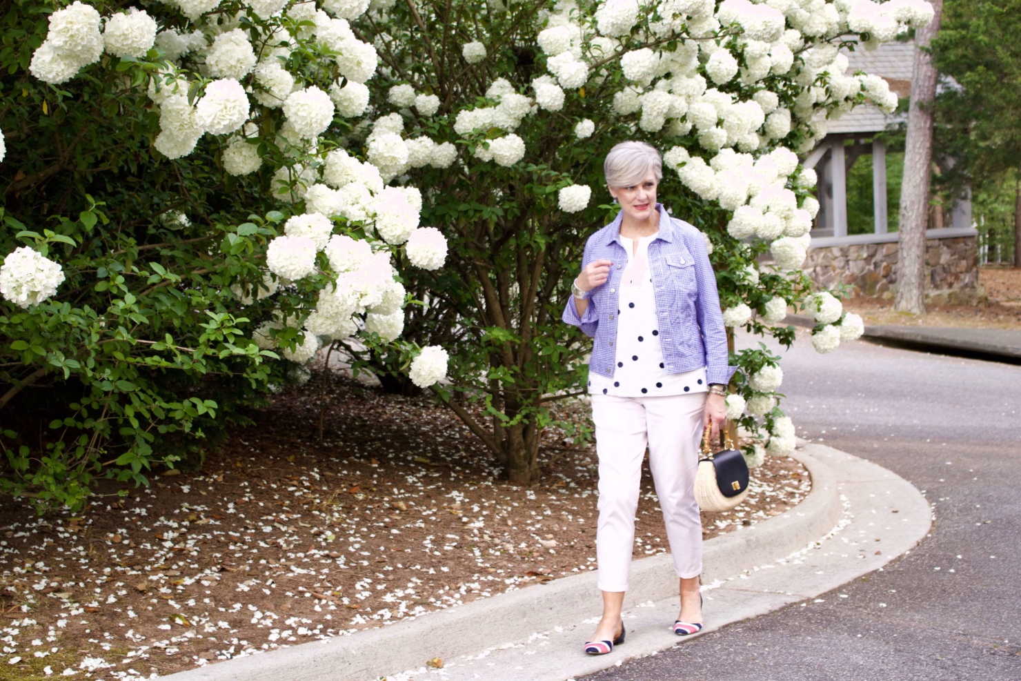 beth from Style at a Certain Age wears a gingham jean jacket, polka dot top, white chinos and wicker handbag