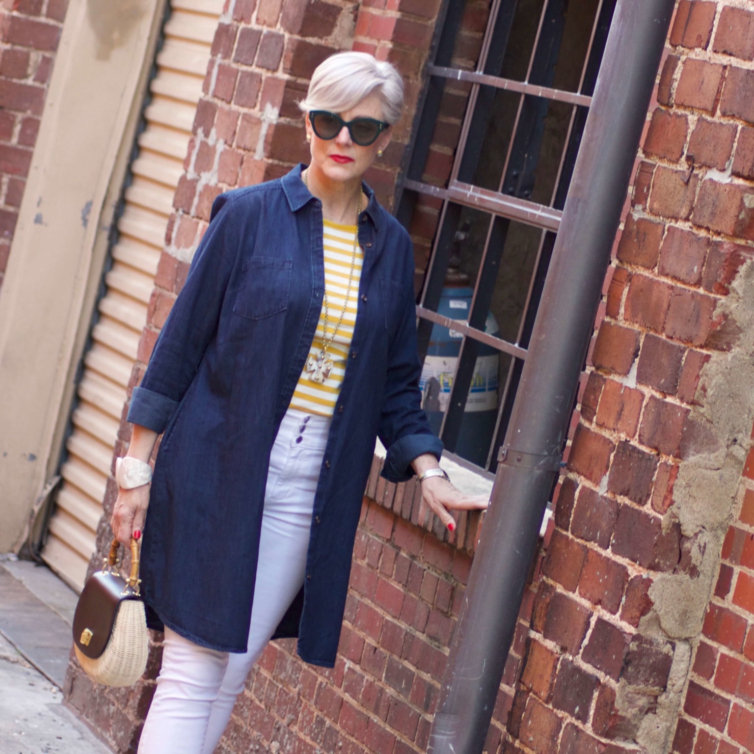 beth from Style at a Certain Age wears a denim duster, striped tee, white denim, suede sandals and wicker handbag