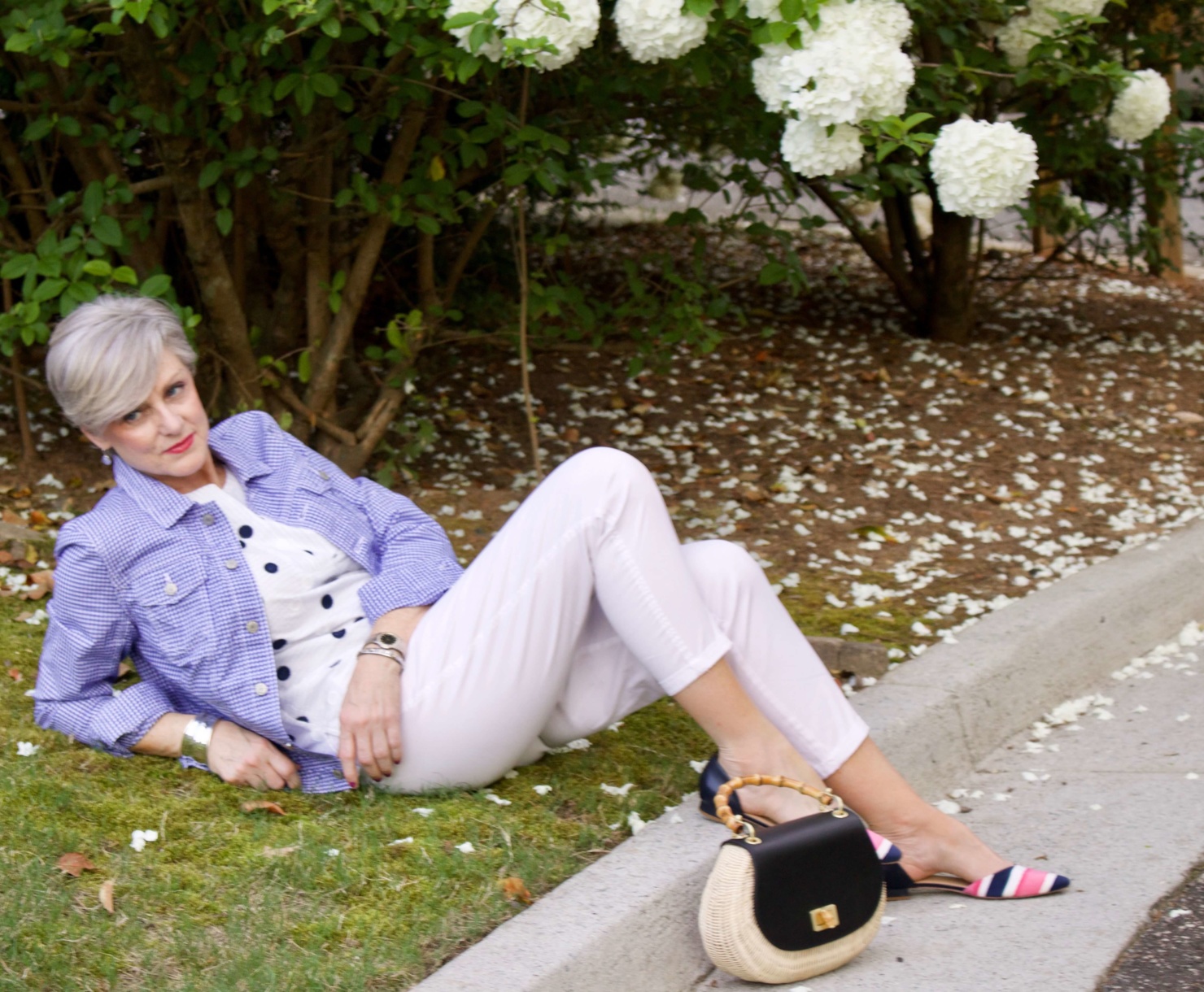 beth from Style at a Certain Age wears a gingham jean jacket, polka dot top, white chinos and wicker handbag