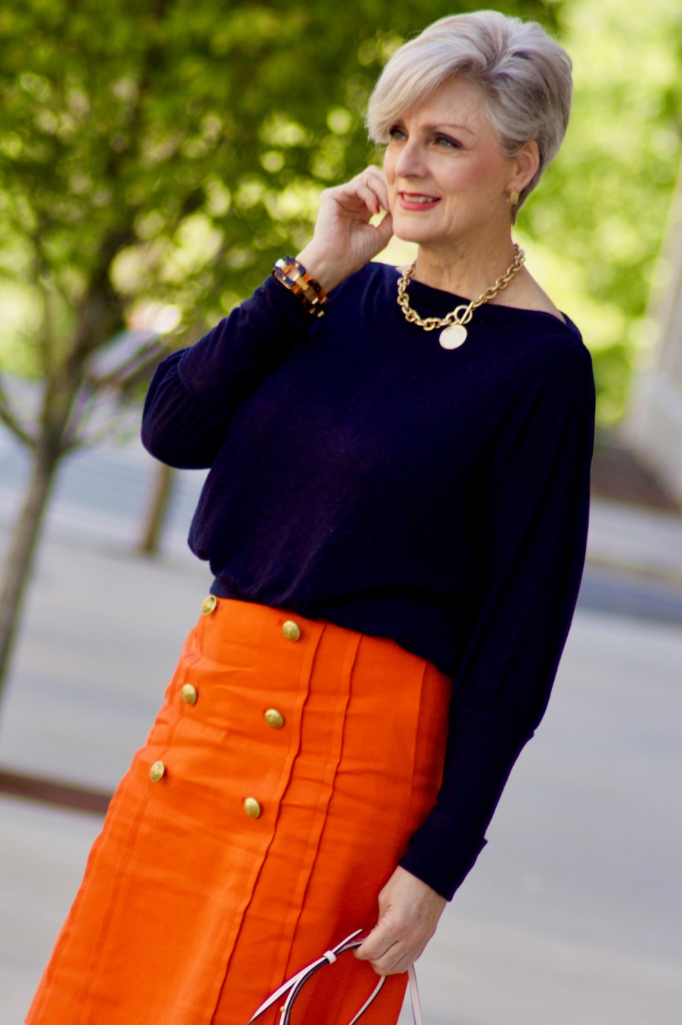beth from Style at a Certain Age wears a J.Crew orange skirt, blue tee, gold sandals, and Tory Burch mini bag.