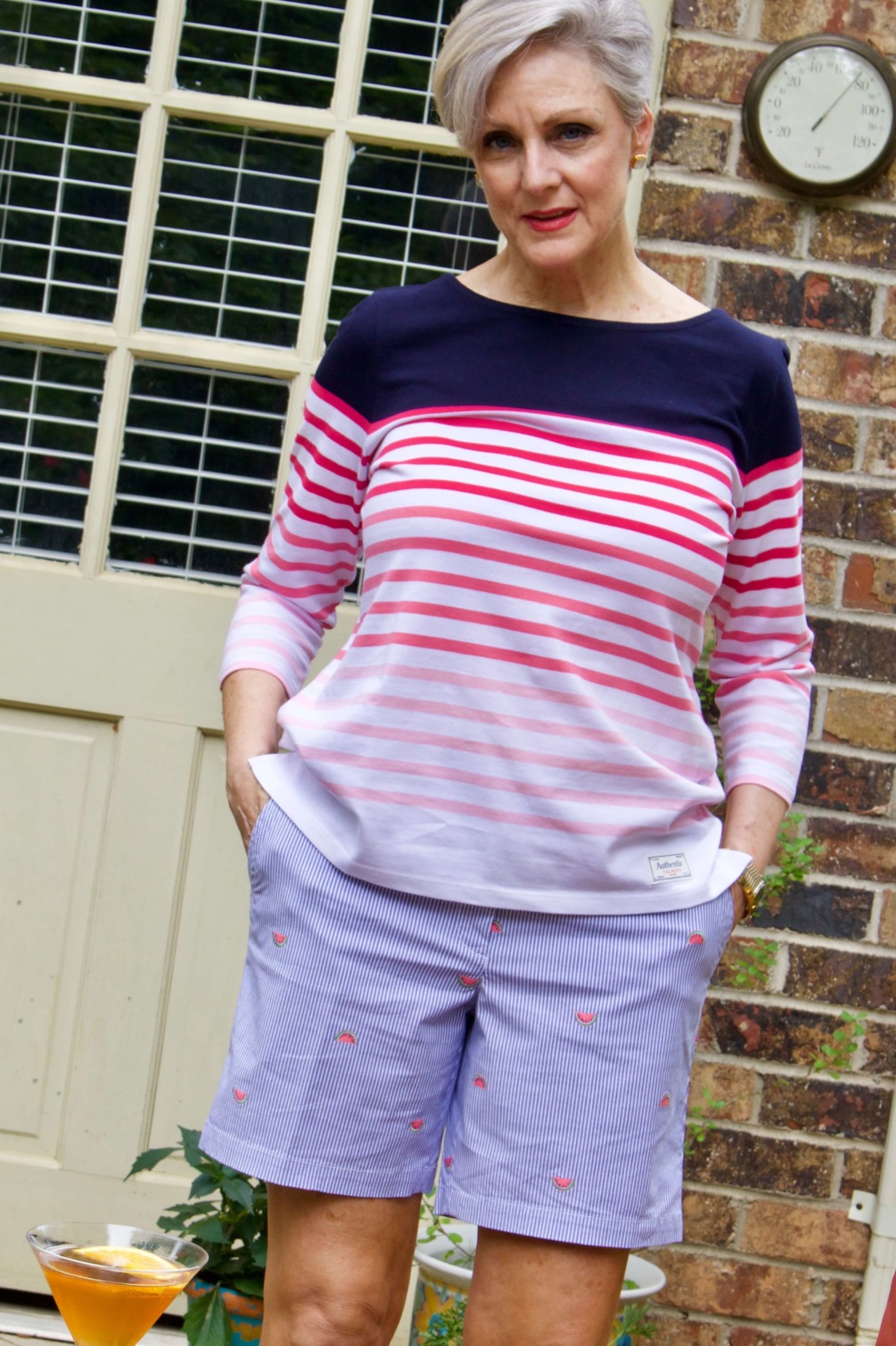 beth from Style at a Certain Age wears watermelon print shorts, striped tee, white jacket and jack rodgers sandals