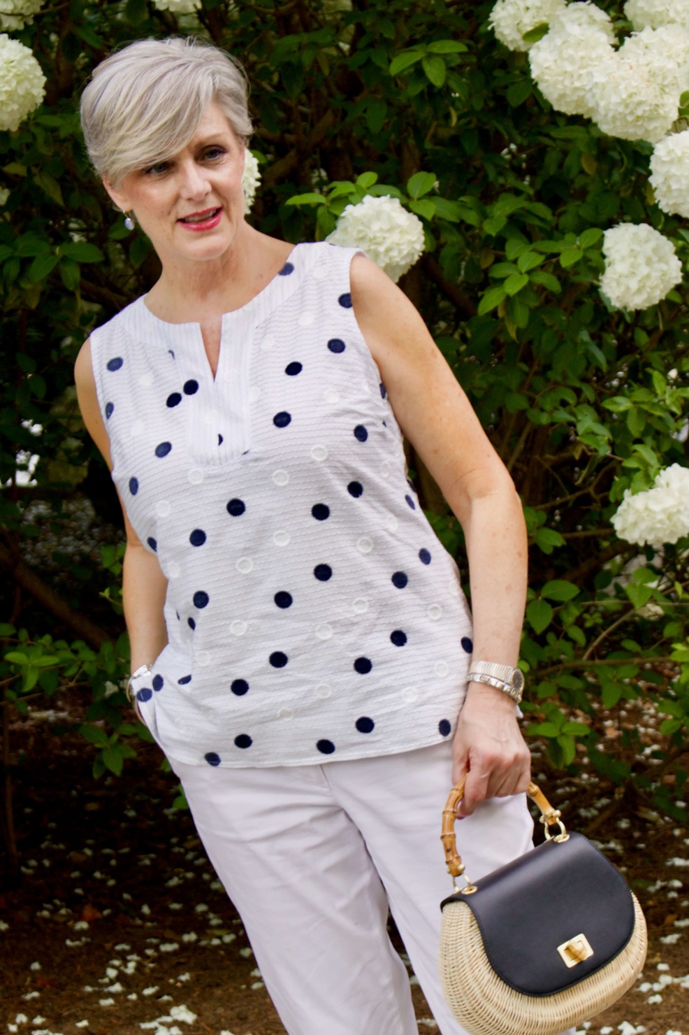 beth from Style at a Certain Age wears a gingham jean jacket, polka dot top, white chinos and wicker handbag