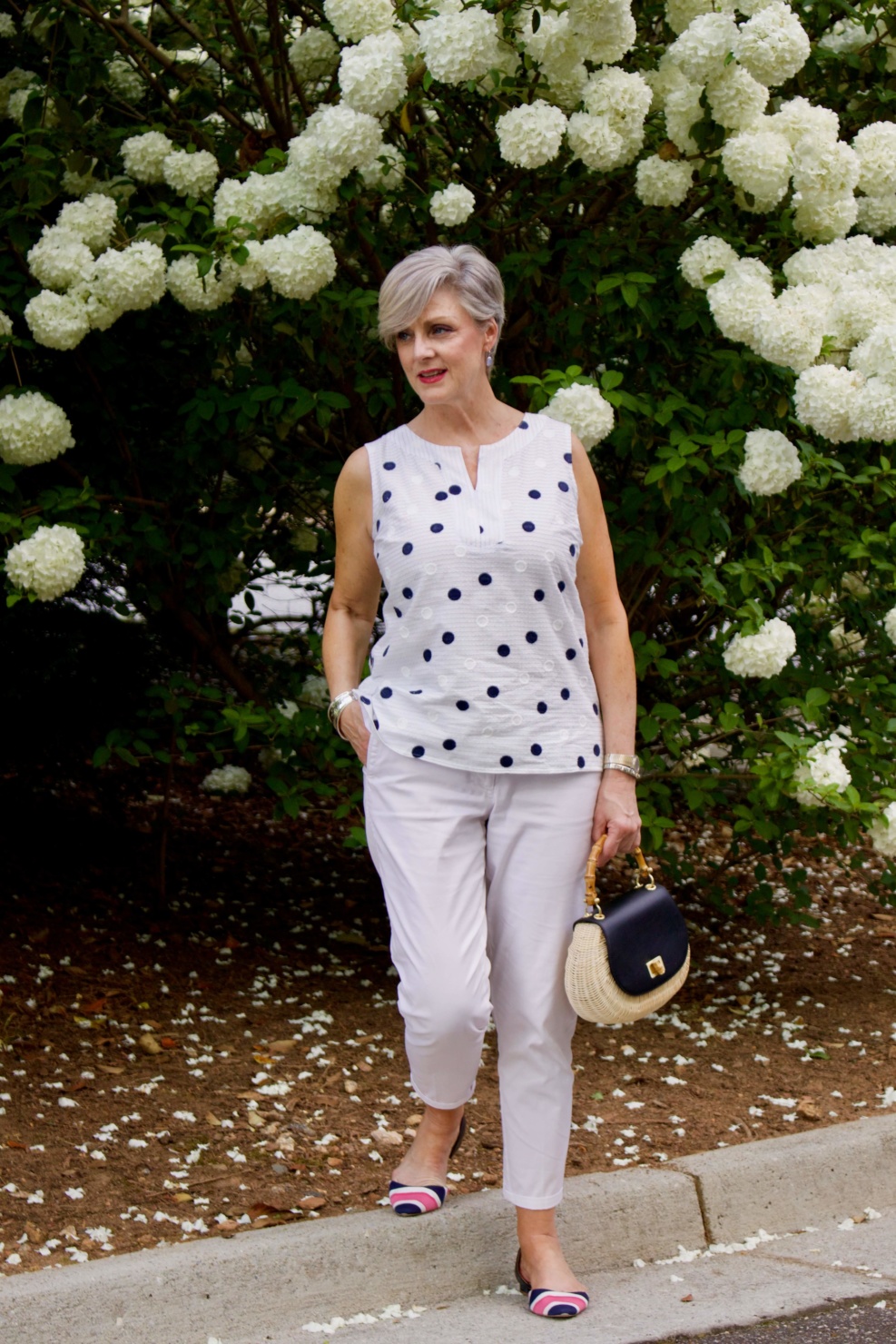 beth from Style at a Certain Age wears a gingham jean jacket, polka dot top, white chinos and wicker handbag