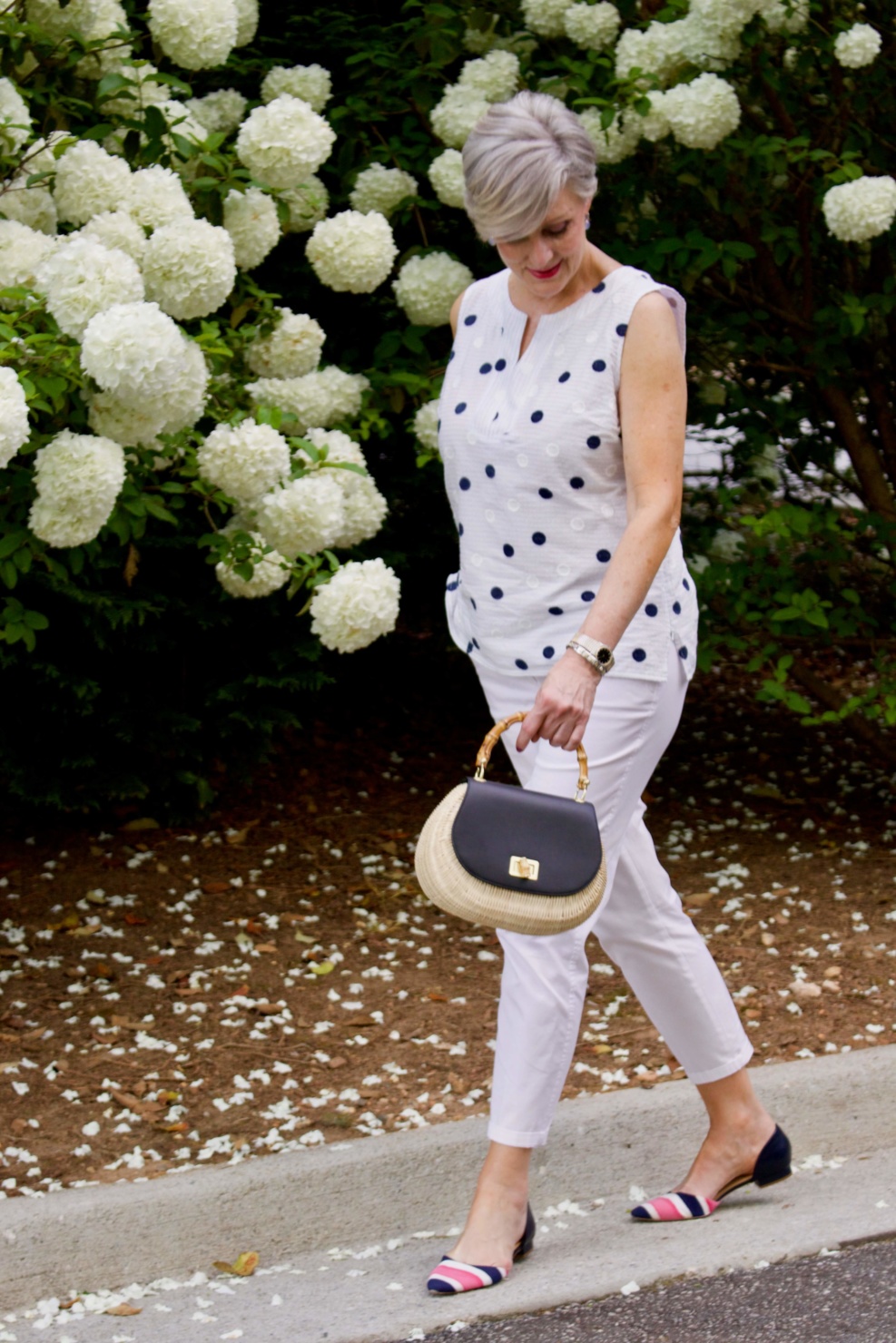 beth from Style at a Certain Age wears a gingham jean jacket, polka dot top, white chinos and wicker handbag
