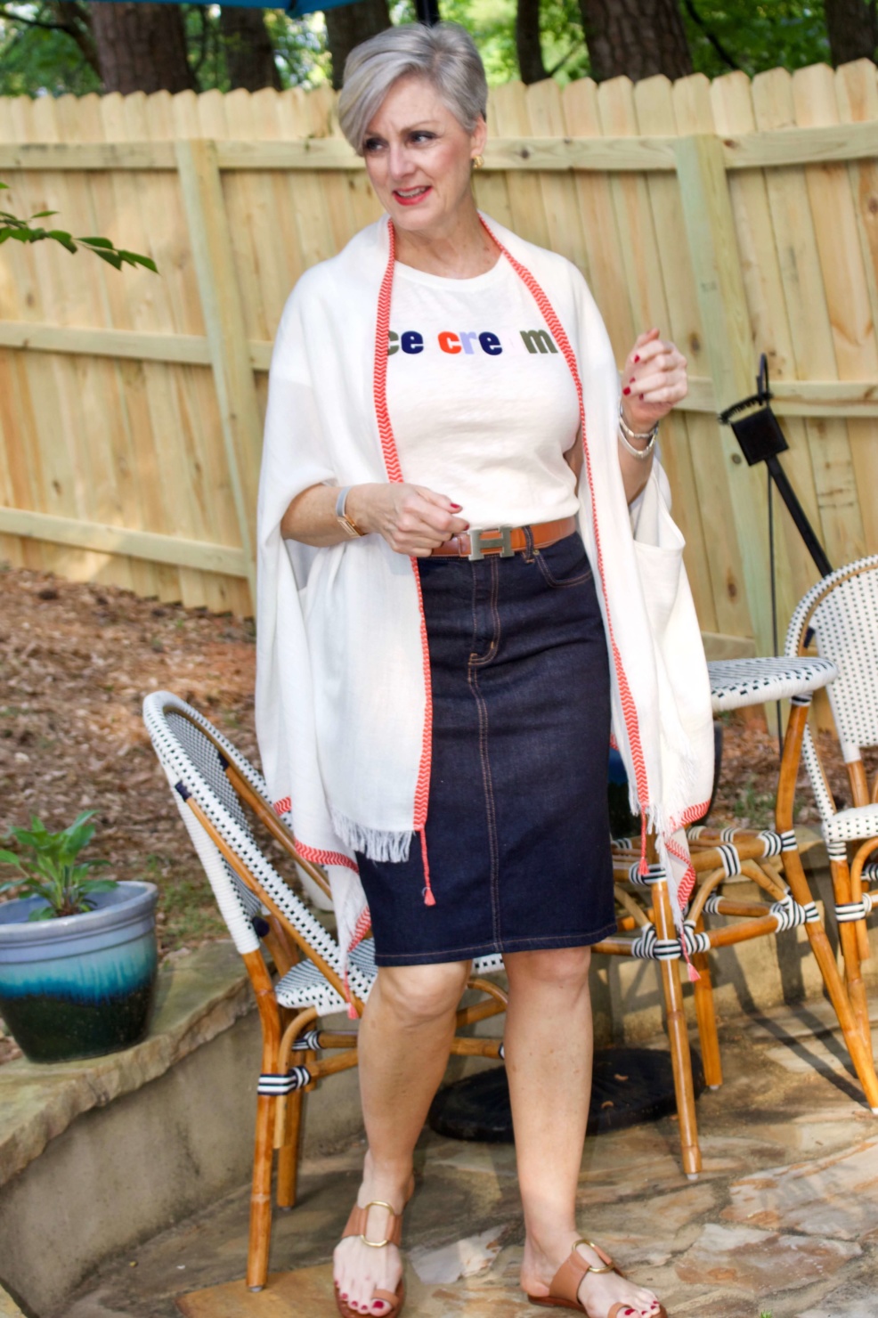 beth from Style at a Certain Age wears a J.Crew graphic tee, jean skirt, lightweight cape scarf, and Tory Burch sandals