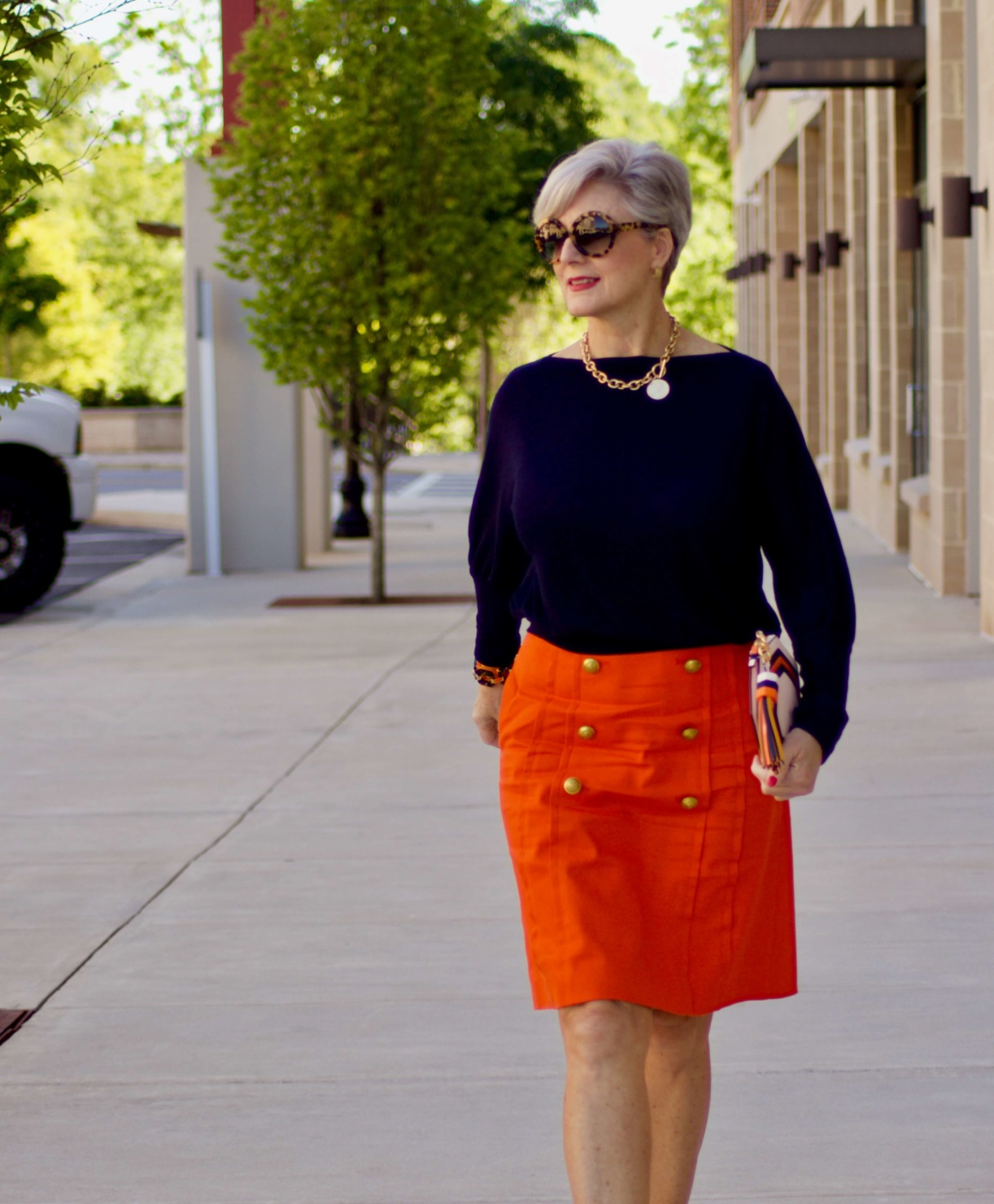 beth from Style at a Certain Age wears a J.Crew orange skirt, blue tee, gold sandals, and Tory Burch mini bag.