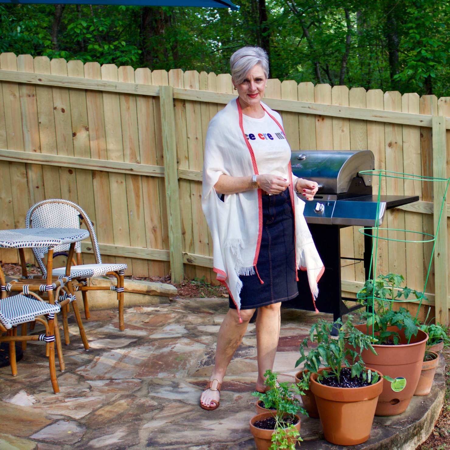 beth from Style at a Certain Age wears a J.Crew graphic tee, jean skirt, lightweight cape scarf, and Tory Burch sandals