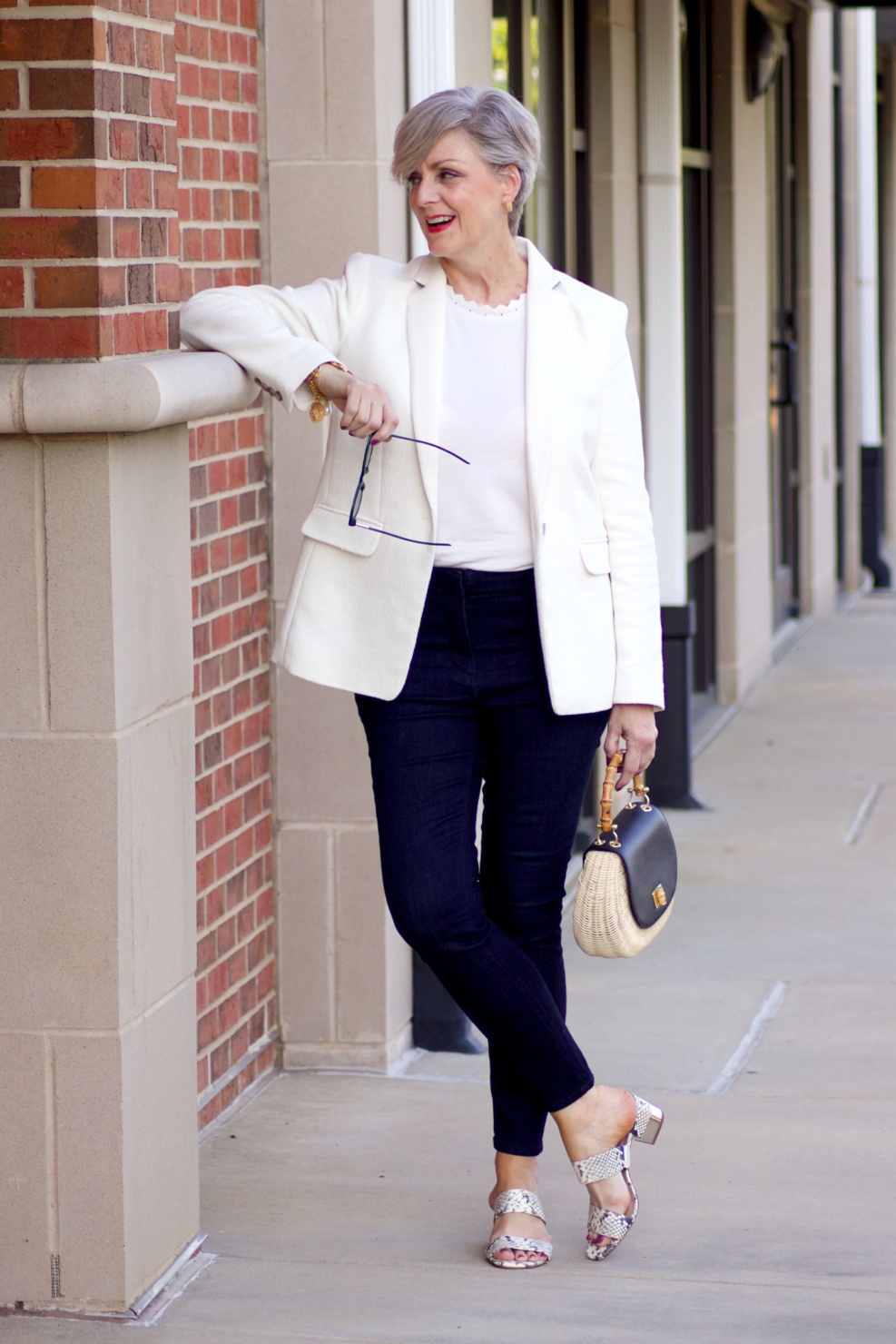 beth from Style at a Certain Age wears a textured ivory blazer, ivory scalloped shell, dark rinse skinny jeans, snakeskin sandals and wicker handbag