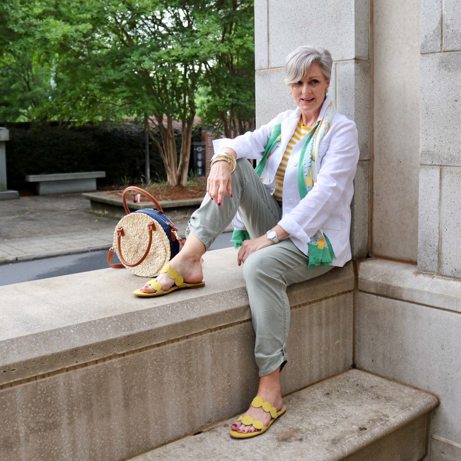 how to wear a jacket for spring and summer beth from Style at a Certain Age wears a white utility jacket, striped tee, green utility pants, yellow sandals, lemon scarf, and cornhusk handbag