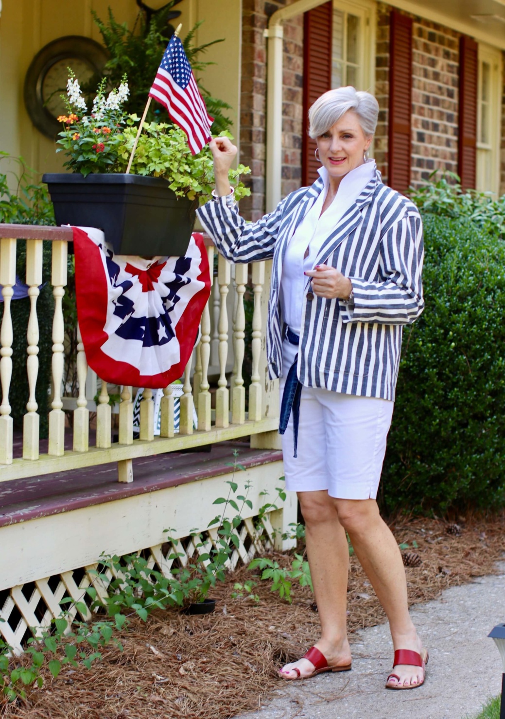 beth from Style at a Certain Age wears a sleeveless white shirt, white boardwalk shorts, striped blazer and red sandals