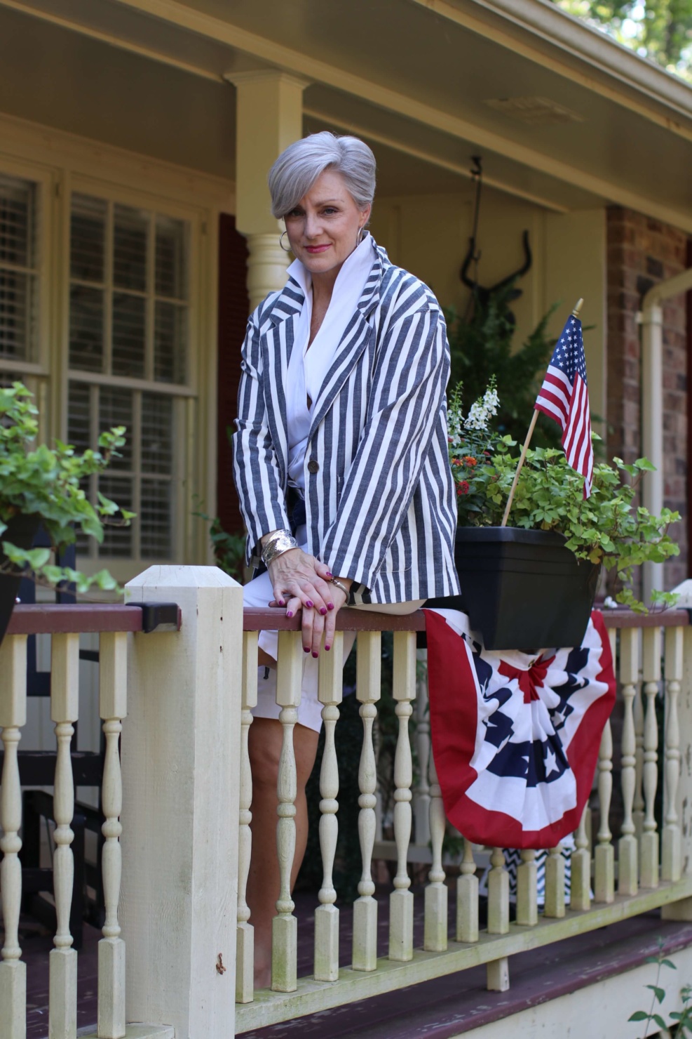 beth from Style at a Certain Age wears a sleeveless white shirt, white boardwalk shorts, striped blazer and red sandals