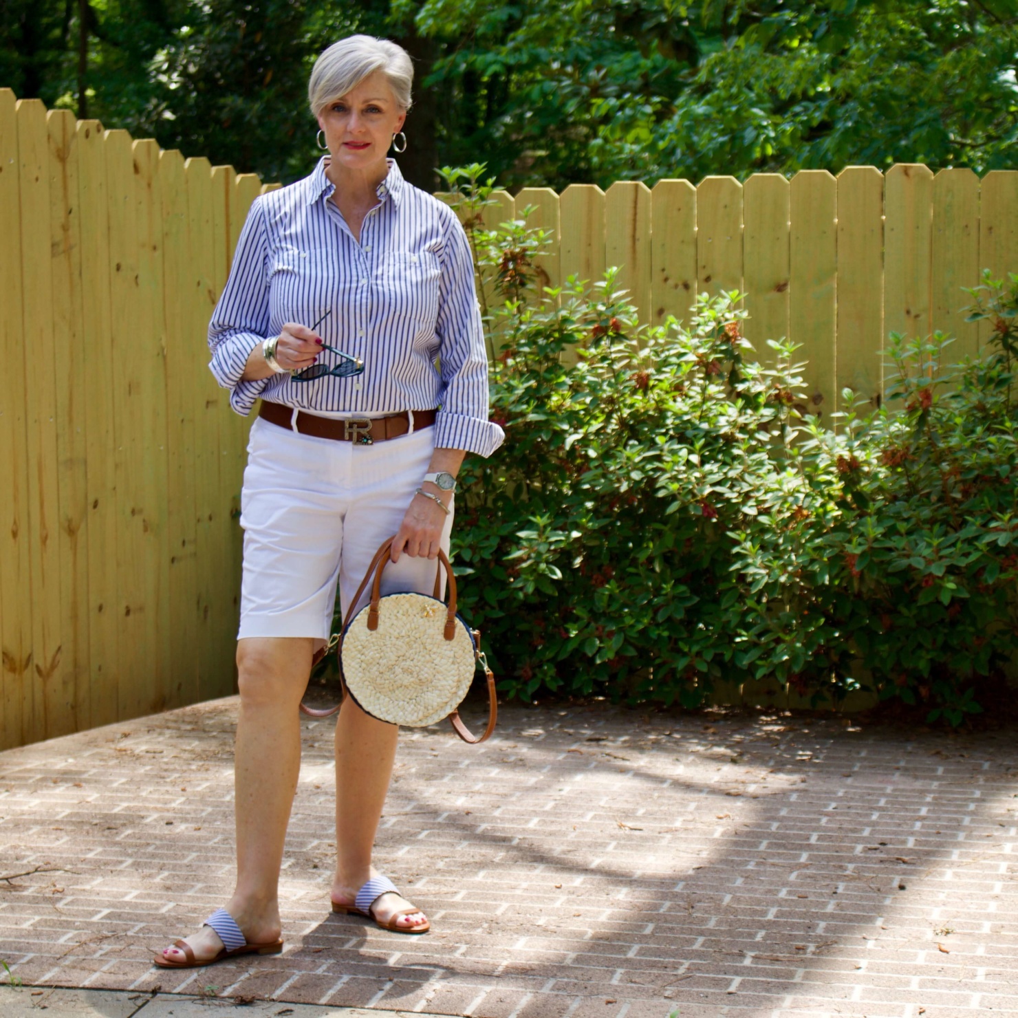 beth from Style at a Certain Age wears a striped shirt, white shorts, sandals, and rattan handbag