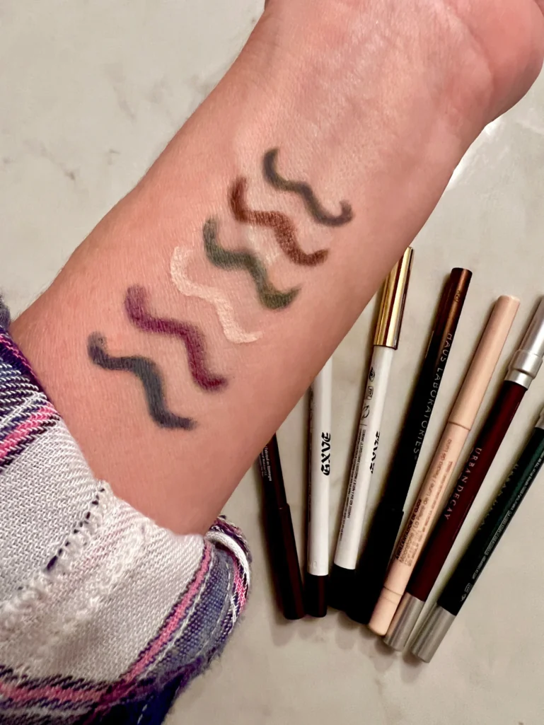 several colors of eye pencil drawn on a forearm to see the colors against natural skin tone