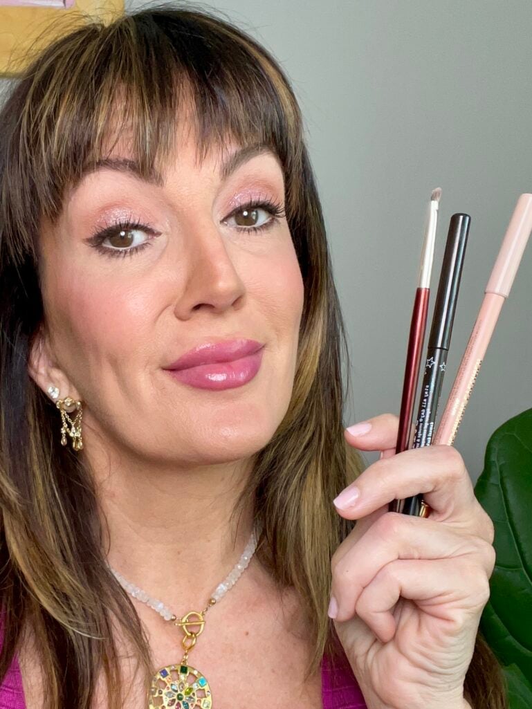 A woman in her 40s shows her finished eye look while holding three eyeliner pencil products