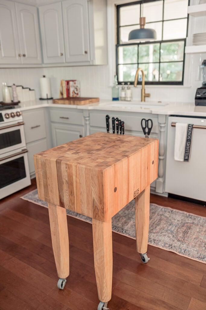 Butcher block island on wheels with wood countertop, books, and wicker storage basket — timeless 2025 kitchen remodel idea.