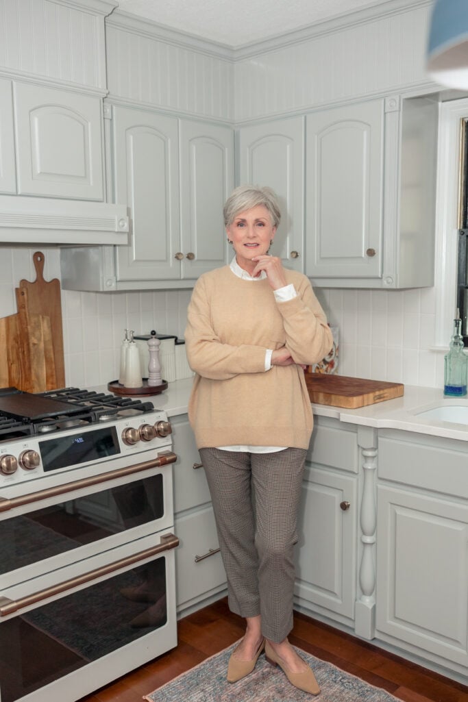 Beth standing in remodeled kitchen with Coventry Gray cabinets, Café Elite dual oven range, and Calcutta Gold Silestone countertops — timeless 2025 remodel.