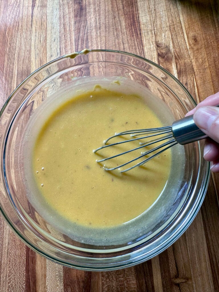 Smooth, thick golden Caesar-style dressing being whisked in a glass bowl