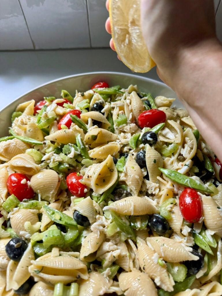 Fresh lemon half being squeezed over the finished seafood pasta salad in a large white serving bowl