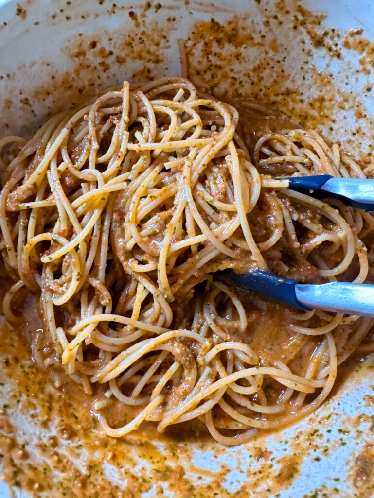 Spaghetti fully tossed and coated in pesto pantesco being mixed with tongs in a large white bowl