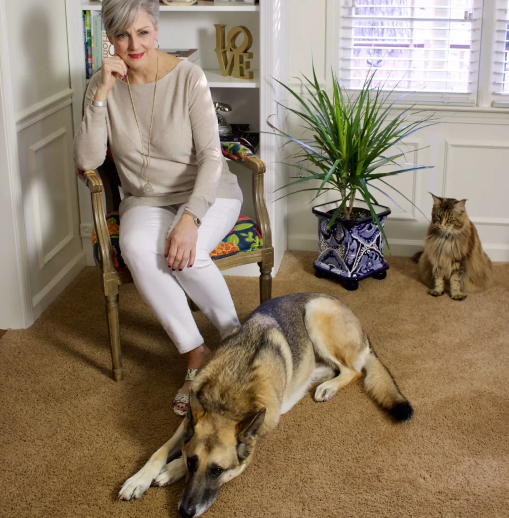 Beth in beige sweater and white pants sitting with Oscar the German Shepherd and Ollie the cat indoors - Fridays with Oscar March 2019