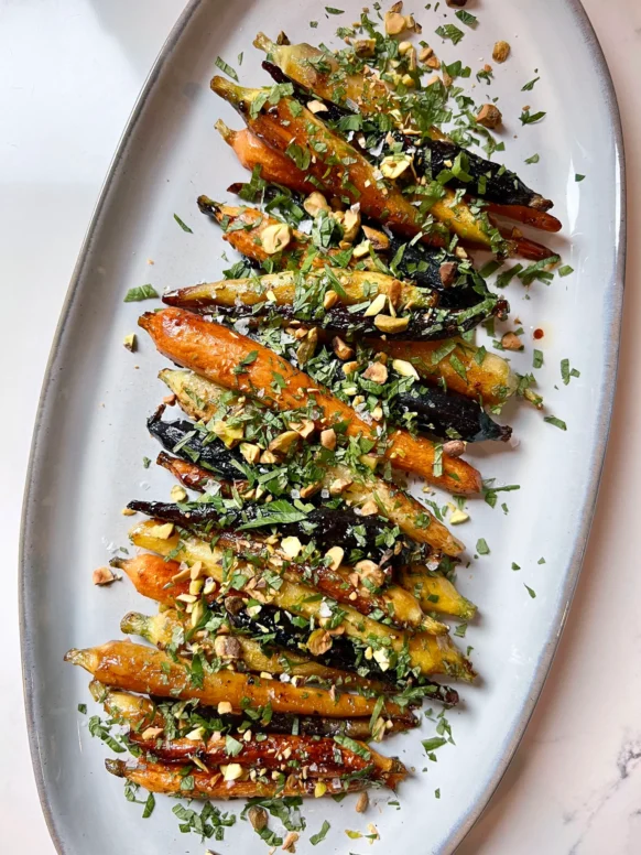 Honey butter roasted carrots with garlic and fresh herbs on a white serving platter