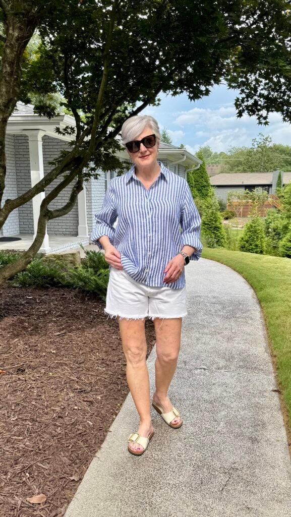 Beth Djalali wears a light blue linen shirt, white jeans, and gold buckle slides—a classic summer outfit formula for women over 50