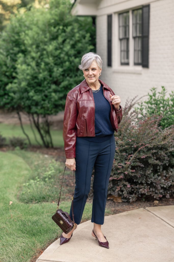 Mature woman in burgundy leather jacket with navy trousers.