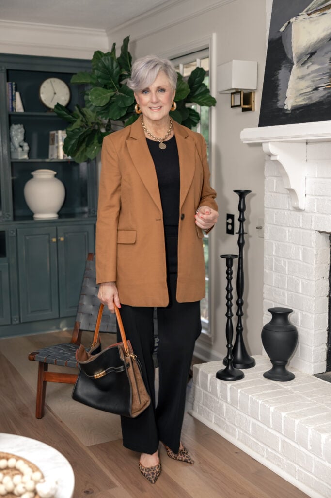 Woman over 50 wearing camel blazer with tailored black trousers and handbag will avoid fall fashion mistakes that make you look old.