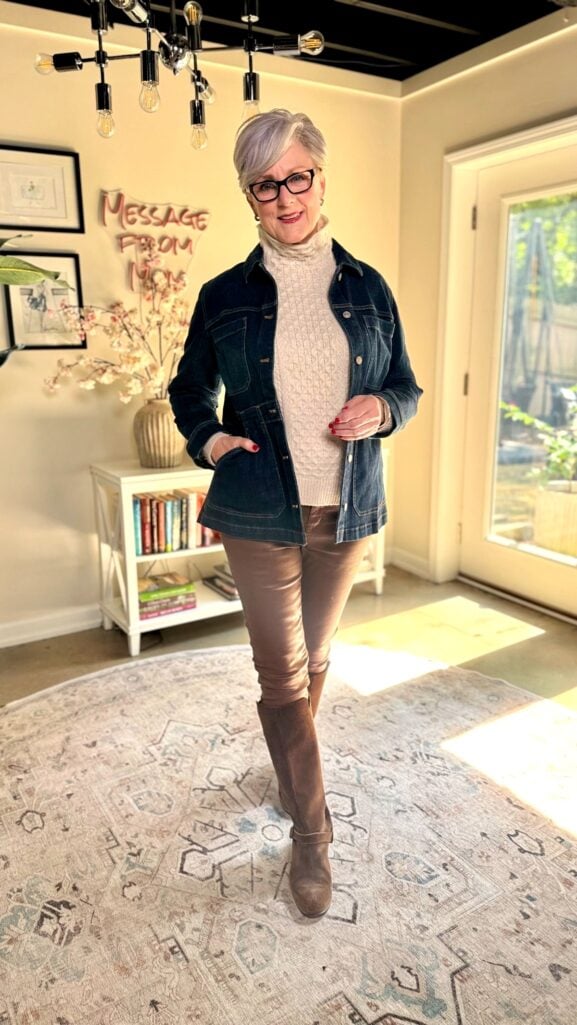 Beth Djalali wearing long denim jacket with cream fisherman sweater and riding boots