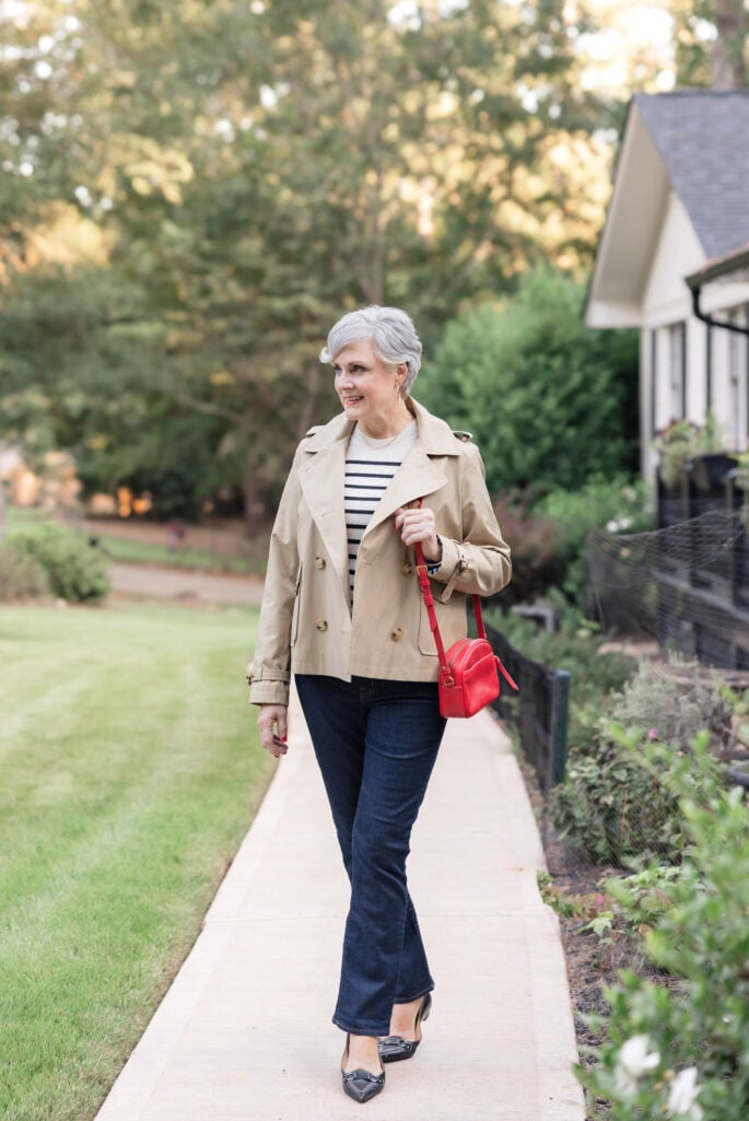 Woman over 50 wearing a cropped trench coat with dark straight-leg jeans.