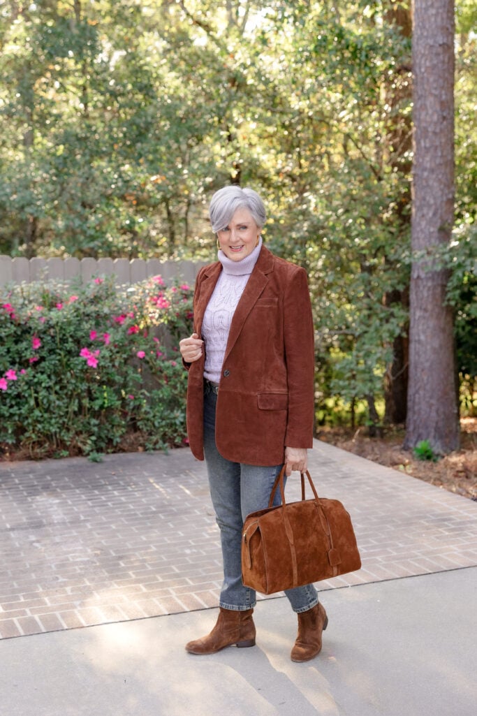 Beth wearing a rust suede blazer, lilac sweater, and gray jeans with brown suede Chelsea boots — warm fall color palette for mature women’s style.